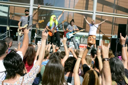 Grupo musical con camisetas de rayas actúa en un escenario ante un público familiar con las manos en alto