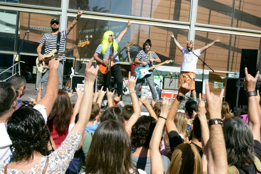Grupo musical con camisetas de rayas actúa en un escenario ante un público familiar con las manos en alto