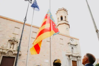 La Senyera ante el campanario de la plaza Mayor de Burriana, con dos falleras en primer plano