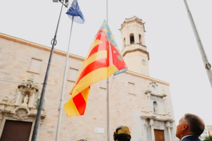 La Senyera ante el campanario de la plaza Mayor de Burriana, con dos falleras en primer plano