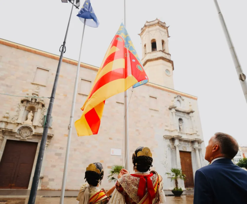La Senyera ante el campanario de la plaza Mayor de Burriana, con dos falleras en primer plano