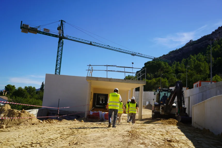 Personas con chalecos y cascos visitan las obras del Centro de Día de Xàtiva, con una grúa al fondo