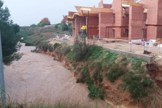 Cauce del barranc d'en Dolça con agua turbia junto a un edificio de ladrillo en construcción en Paterna