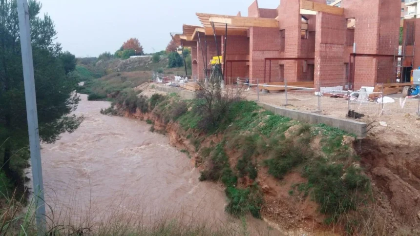 Cauce del barranc d'en Dolça con agua turbia junto a un edificio de ladrillo en construcción en Paterna