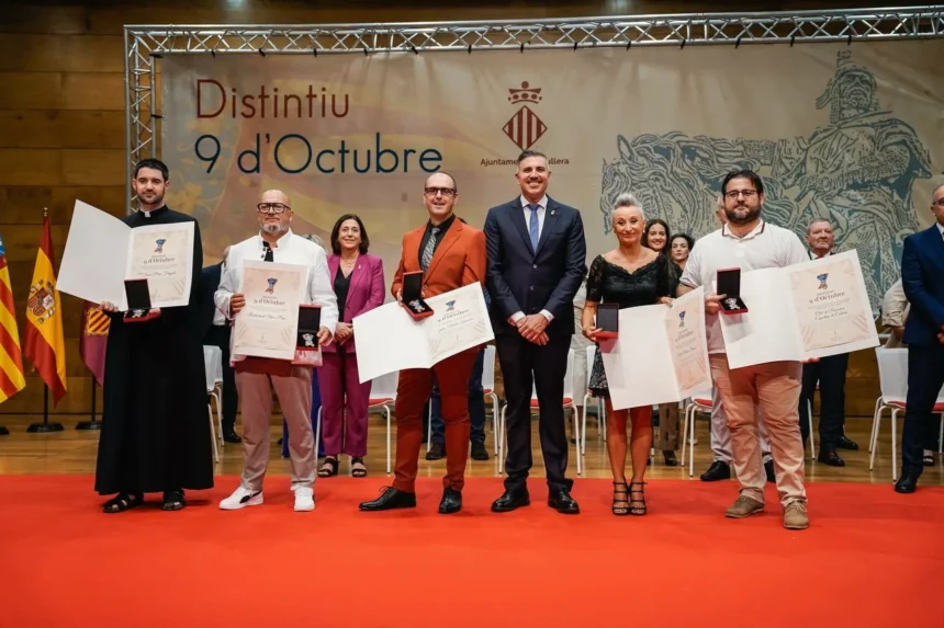 Los galardonados con los Distintius 9 d’Octubre de Cullera posan con sus diplomas y medallas ante el cartel del acto