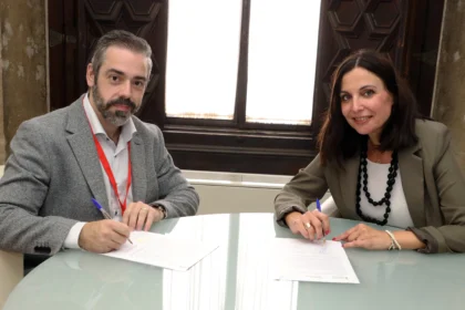 Un hombre y una mujer firman un convenio sentados ante una mesa de cristal