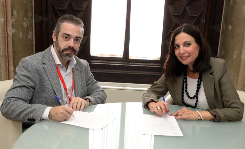 Un hombre y una mujer firman un convenio sentados ante una mesa de cristal