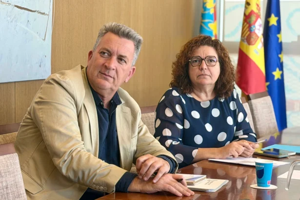 Dos responsables institucionales sentados ante una mesa, con las banderas de la Comunitat Valenciana, España y la Unión Europea al fondo
