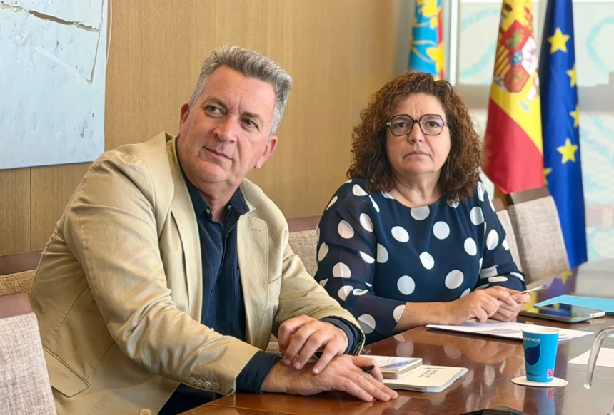 Dos responsables institucionales sentados ante una mesa, con las banderas de la Comunitat Valenciana, España y la Unión Europea al fondo