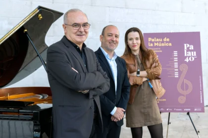 Tres personas posan junto a un piano y un cartel del 40 aniversario del Palau de la Música de València