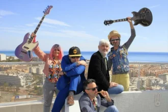 Cinco músicos posan en una azotea con una guitarra y un bajo en alto, con el mar al fondo