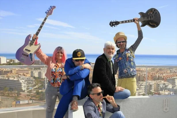 Cinco músicos posan en una azotea con una guitarra y un bajo en alto, con el mar al fondo