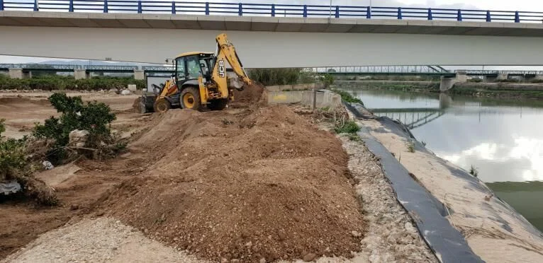 Retroexcavadora trabajando en la orilla de un cauce junto a un puente en Sueca