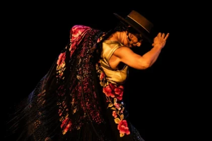 Bailaora de flamenco con sombrero cordobés y mantón de flores bordadas sobre fondo negro