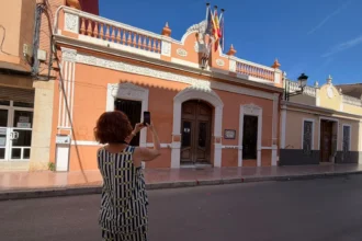 Una mujer fotografía con su teléfono móvil la fachada de un edificio de colores anaranjados